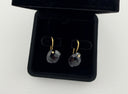 Black onyx checker cut heart drop earrings with gold hook closures laid flat on a light grey surface, showing the faceted stone detail and gold bezel setting.