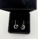 Black onyx checker cut heart drop earrings with gold hook closures laid flat on a light grey surface, showing the faceted stone detail and gold bezel setting.