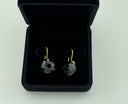 Black onyx checker cut heart drop earrings with gold hook closures laid flat on a light grey surface, showing the faceted stone detail and gold bezel setting.
