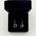 Black onyx checker cut heart drop earrings with gold hook closures laid flat on a light grey surface, showing the faceted stone detail and gold bezel setting.
