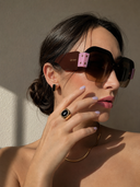 Woman wearing sunglasses with a minimal background and black onyx ring and earrings
